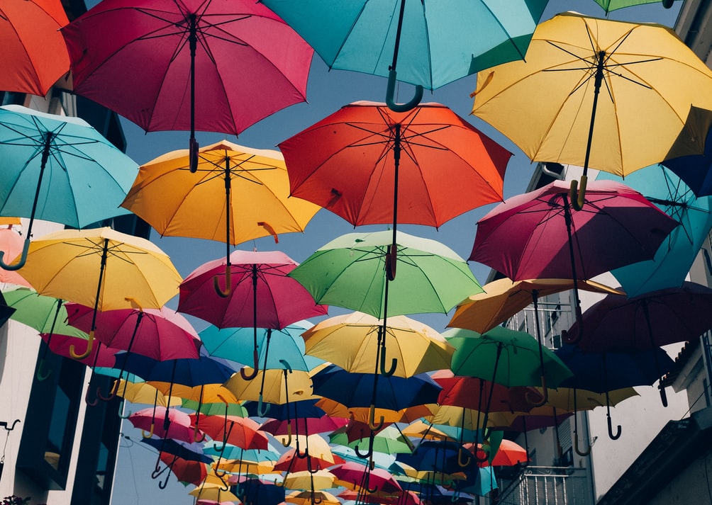 Värikkäitä sateenvarjoja roikkumassa naruista vasten taivasta, kuva taideinstallaatiosta.